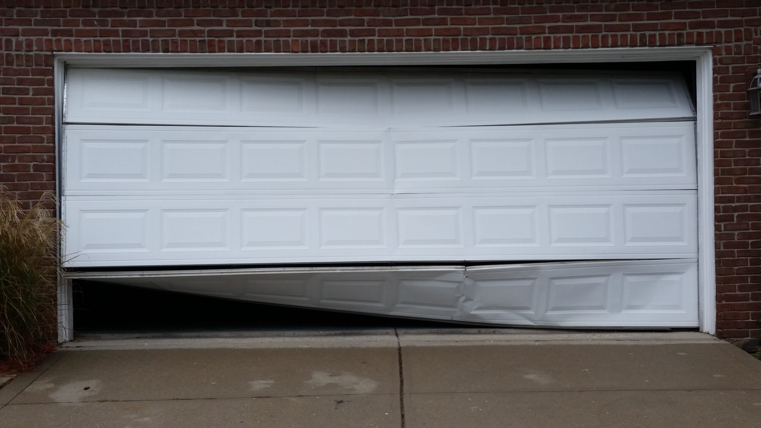 White garage door with severe impact damage, bent panels, and sections pushed off track
