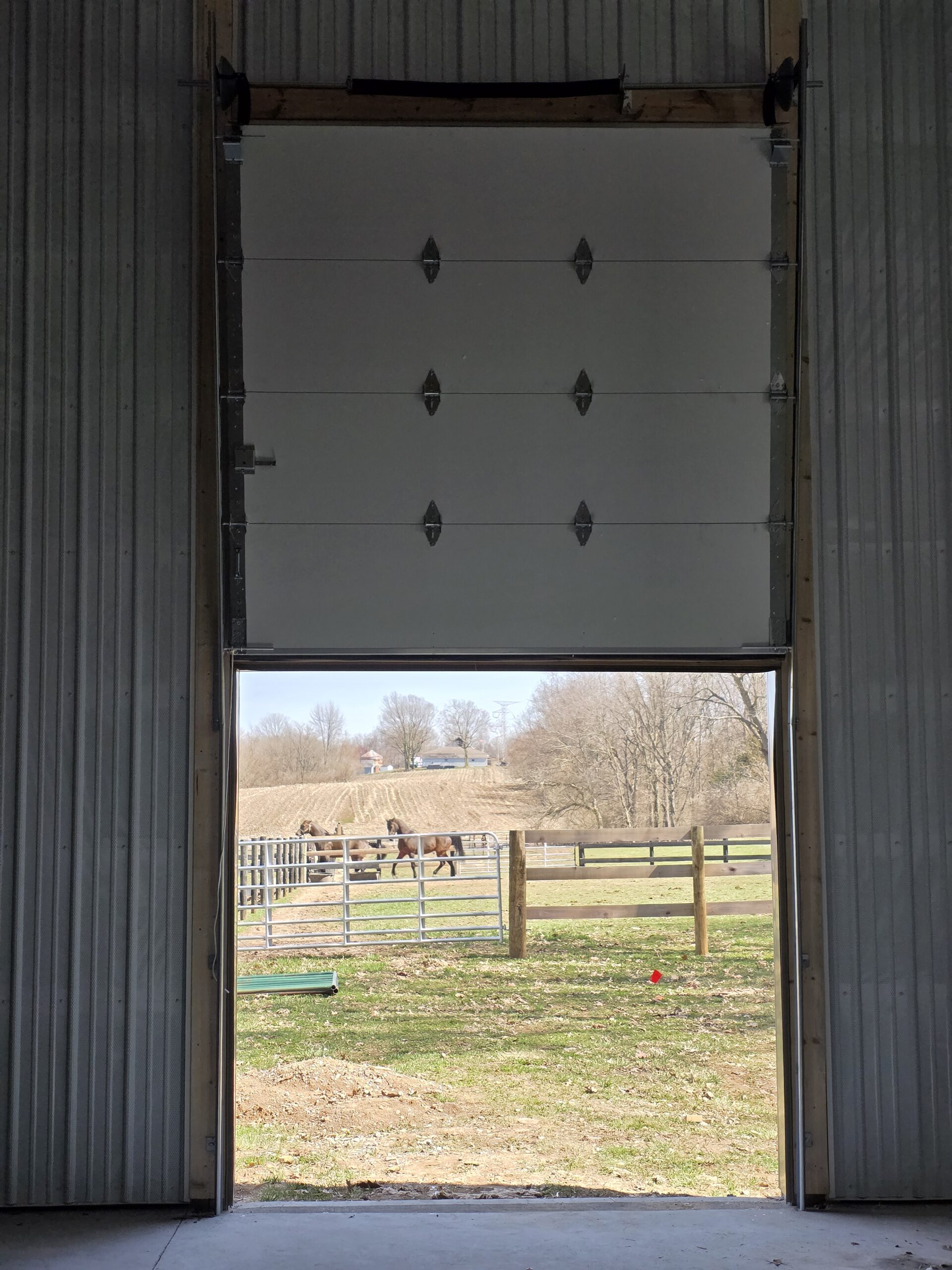 Newly installed vertical lift garage door in a metal building, fully open with outdoor farm area visible